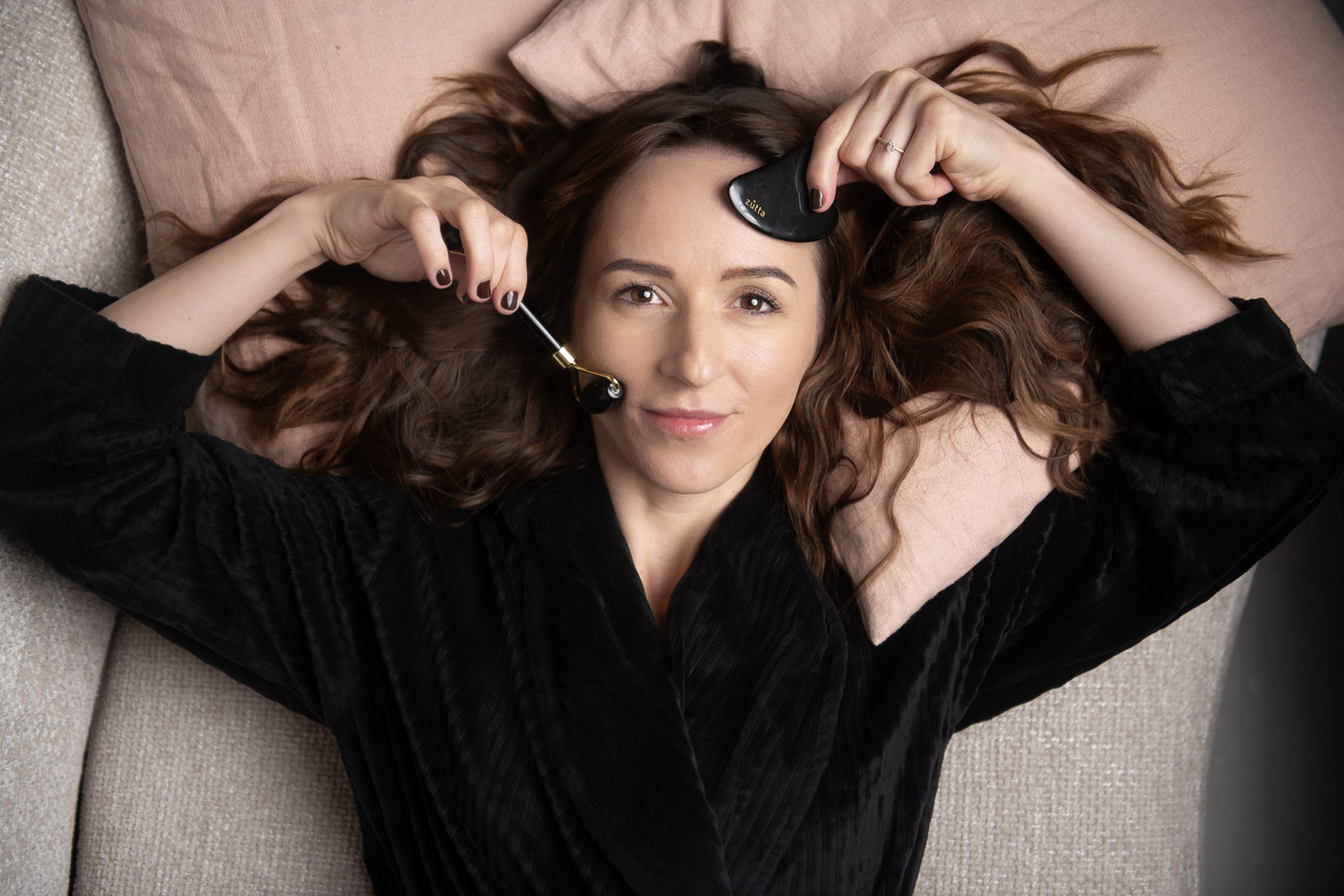 Woman receiving facial massage with gua sha stone and roller in a relaxed spa setting